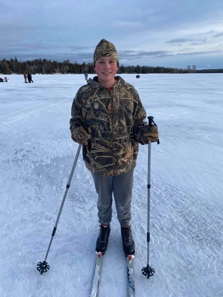 Boy cross-country skiing on the frozen lake at dusk