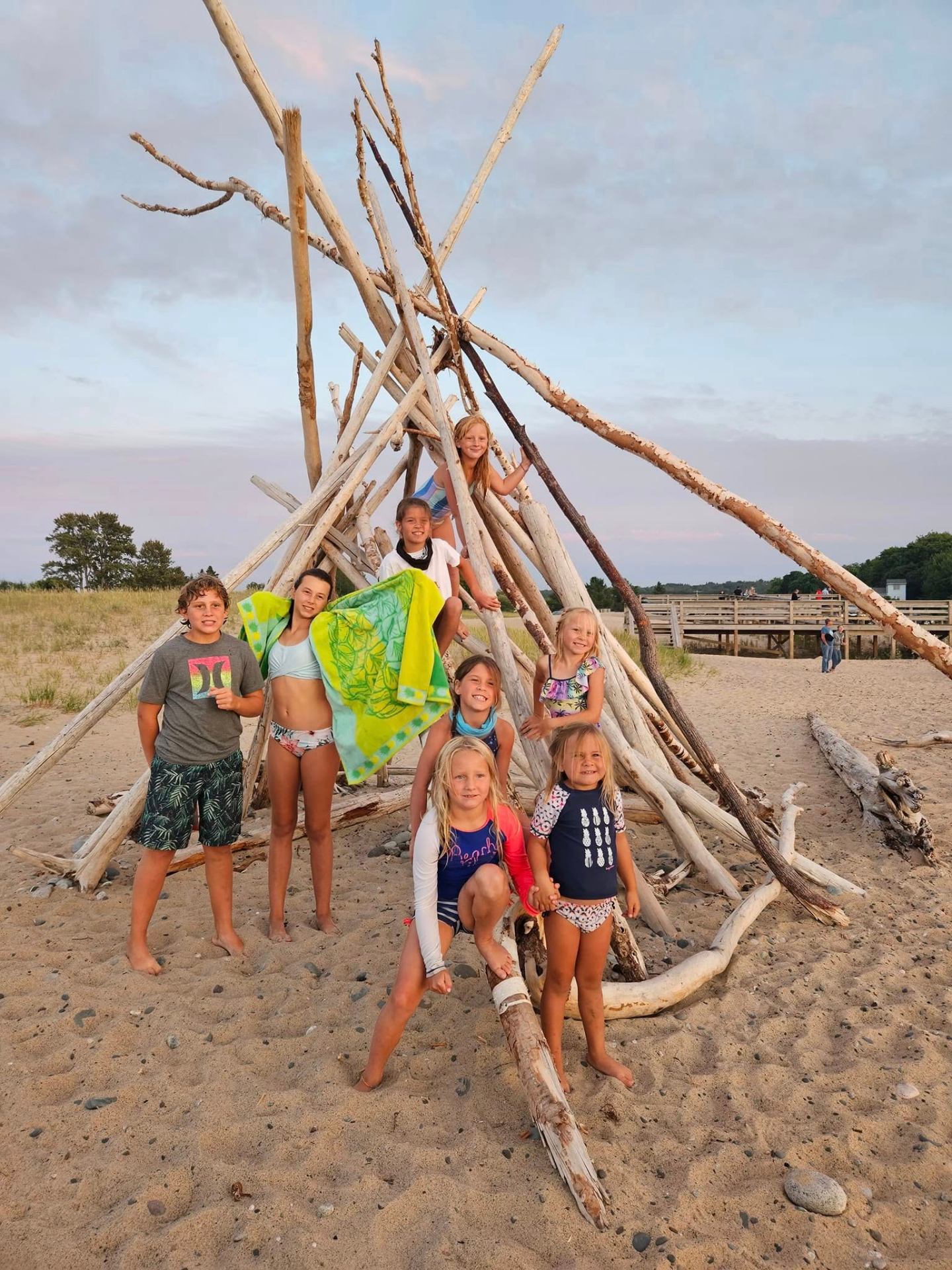 Kids playing on a driftwood teepee on the beach at sunset