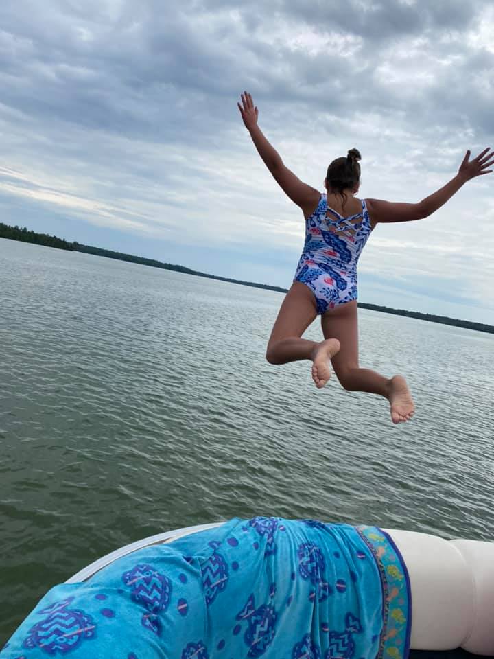 Girl jumping off a pontoon boat into the lake